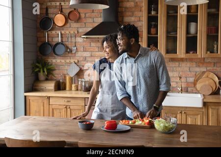 Happy dreamy African American couple cooking in kitchen together Stock Photo