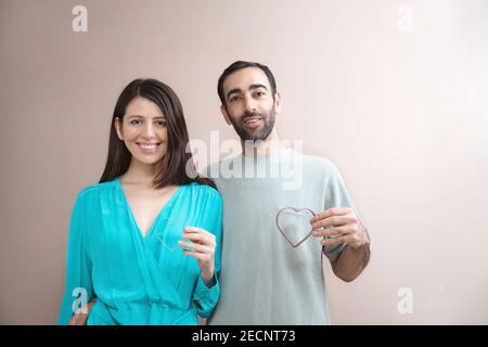 Young adult man and woman hold hearts, looking at camera. Showing love, care, smiling. Mixed race, brown hair. Attractive people, closeup portrait. Cr Stock Photo