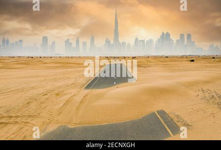 View from above, stunning aerial view of a deserted road covered by sand dunes with the Dubai Skyline in the background. Dubai, United Arab Emirates. Stock Photo