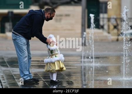 Valletta, Malta. 13th Feb, 2021. A man holds a girl dressed up for carnival to watch a fountain in Valletta, Malta, on Feb. 13, 2021. Maltese carnival enthusiasts do not let the COVID-19 pandemic dampen their passion for carnival as they still work on their colorful floats and exhibit them in a static art installation rather than a parade, in line with pandemic restrictions. Credit: Jonathan Borg/Xinhua/Alamy Live News Stock Photo