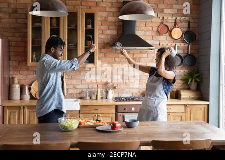 Funny African American couple pretending fighting with kitchenware, having fun Stock Photo