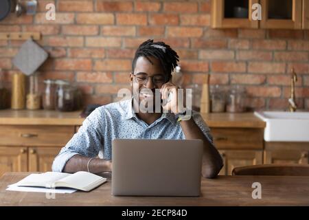 Smiling African American man talking on phone, using laptop Stock Photo