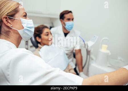 Female dentist wearing face mask showing x-ray to patient. Dental expert explaining the treatment procedure to female patient in clinic. Stock Photo