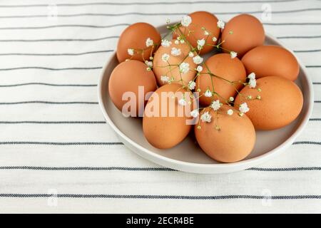 Closeup view of clay plate full of many raw whole brown chicken eggs for cooking fresh homemade food . Stock Photo