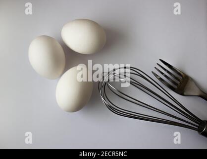 three chicken white eggs whisk and fork on gray background Stock Photo