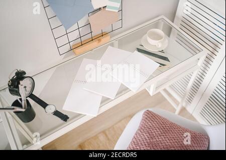 Background image of empty home cozy office working space modern scandinavian design. White glass table, holder lattice for notes with stylish decor elements, stationery, alarm clock and wristwatch Stock Photo