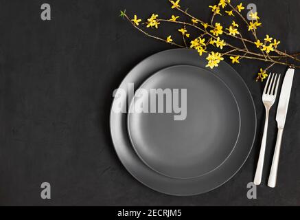 Black table setting. Yellow flowers and black plate on a dark gray background. Easter. Copy space, top view, flat lay. Stock Photo