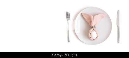 Beautiful Easter table setting with a white egg on a pink napkin with rabbit ears on a white background. Banner. Easter concept. Space for text. Stock Photo