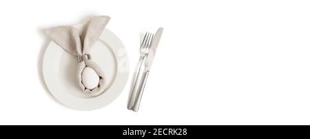 Easter table decorations with egg in a gray Easter bunny napkin on a white background. Banner. Table setting. Copy space. View from above. Stock Photo
