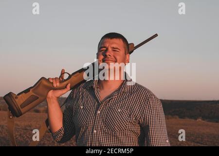 Middle-aged man in plaid shirt with rifle, Middle-aged man in a plaid shirt with a rifle, twilight. Stock Photo