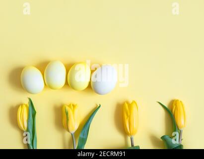 Easter decorations with yellow eggs and tulip flowers on a yellow background. Easter card. View from above. Space for text. Stock Photo