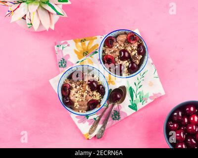 Chocolate ice cream with sprinkles, nuts and fresh cherries on pink Stock Photo