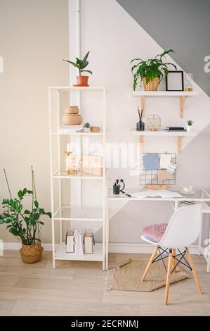Background image of empty home office working space in a cozy apartment with modern scandinavian design. White table chair shelving with stylish decor elements, stationery, houseplants in wicker pots Stock Photo