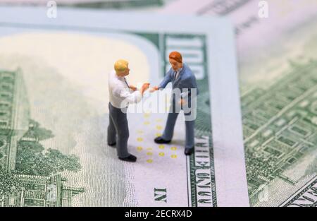 Businessmen figurines shaking hands on cash. Tiny businessmen models on money background. Finance or economic growth concept. Making profitable deal. Stock Photo