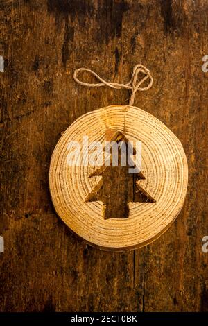 Crafted wooden ornament shaped like a Christmas tree hangs elegantly from a natural twine string against a rustic wooden background Stock Photo
