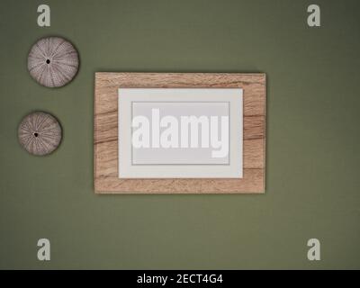 White frame mockup on wooden board, two sea urchin shells on green background. Flat lay, overhead view. Stock Photo