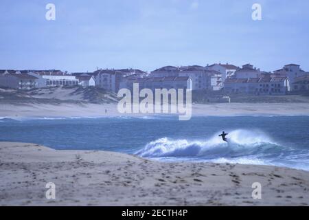 A surfer sportingly rides down a wave during sunset on a beach in Portugal on the Atlantic Ocean Stock Photo