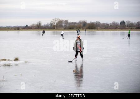 People ice skate on frozen flooded fields near Ely in Cambridgeshire, as the cold snap continues to grip much of the nation. Picture date: Sunday February 14, 2021. The Cambridgeshire Fens were the birthplace of British speed skating and require four nights of frost, with a temperature of -4 or colder and little or no thawing during the days in between, to make ice strong enough to skate on. Stock Photo
