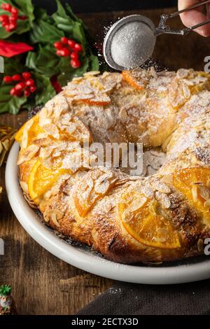 Top view of Roscon de Reyes, freshly made, with Christmas decorations and dark background, vertical Stock Photo