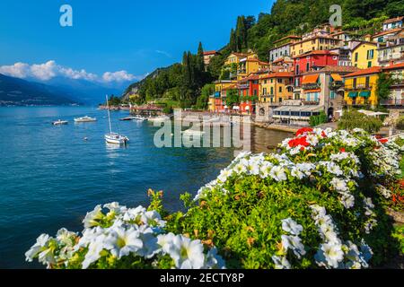 Flowery fence and colorful mediterranean buildings on the waterfront. Anchored boats in the harbor of Varenna, lake Como, Lombardy, Italy, Europe Stock Photo