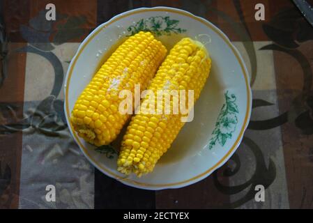 Tasty yellow boiled Ukrainian two pumpkins of corn and salt laid out on plates with green flowers. Stock Photo
