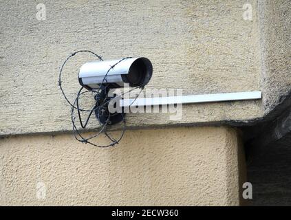 Security camera covered entangled in barbed wire mounted on the rough house wall in the in a disadvantaged district side view close up Stock Photo