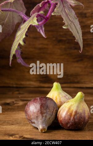 View of three figs with leaves of purple gynura plant, on wooden table, vertical Stock Photo