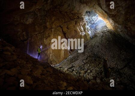 Man lighting a cave with headlamp, exploring dark underground limestone cave Stock Photo