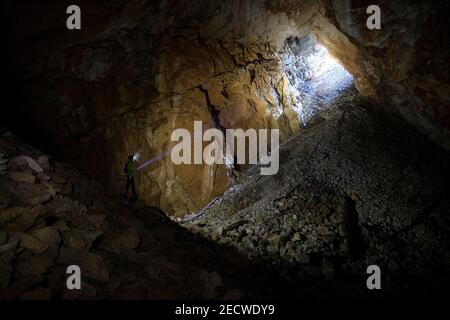 Man lighting a cave with headlamp, exploring dark underground limestone cave Stock Photo