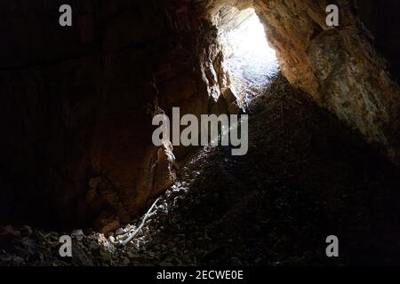 Man lighting a cave with headlamp, exploring dark underground limestone cave Stock Photo