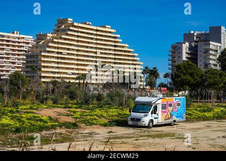 Colourful camper van parked on waste ground, apartment blocks and palm trees a the popular holiday destination of Calpe, Costa Blanca, Alicante, Spain Stock Photo