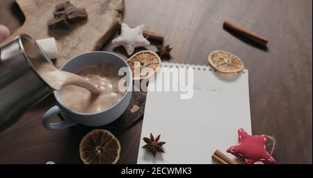 pour hot chocolate into blue cup with new year goals list in notepad, wide photo Stock Photo