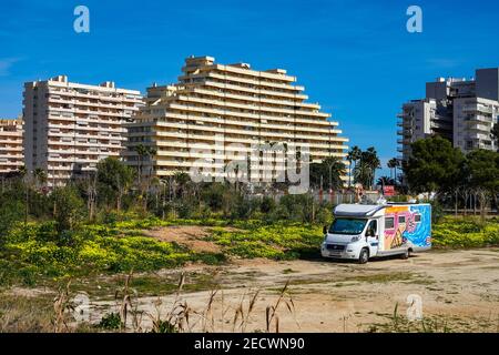 Colourful camper van parked on waste ground, apartment blocks and palm trees a the popular holiday destination of Calpe, Costa Blanca, Alicante, Spain Stock Photo