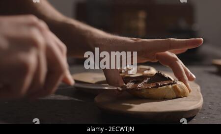 man spreading chocolate spread on baguette slices on olive board, wide photo Stock Photo