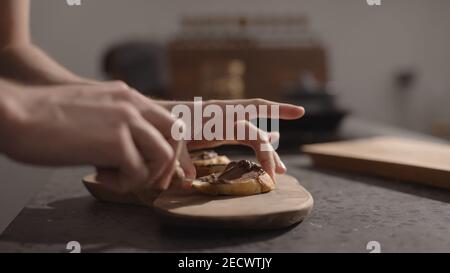 man spreading chocolate spread on baguette slices on olive board, wide photo Stock Photo