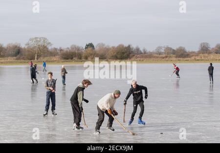 People play ice hockey on frozen flooded fields near Ely in Cambridgeshire, as the cold snap continues to grip much of the nation. Picture date: Sunday February 14, 2021. The Cambridgeshire Fens were the birthplace of British speed skating and require four nights of frost, with a temperature of -4 or colder and little or no thawing during the days in between, to make ice strong enough to skate on. Stock Photo
