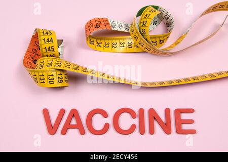 vaccine word written in red with a measuring tape on light pink background Stock Photo