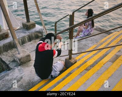 A couple takes pictures in front of the sea near Tsing Ma Bridge.On Valentine’s Day, people are celebrating under the influence of COVID-19. Many choose to spend with their loved ones at the countryside where they are fewer people to give better social distancing. Stock Photo