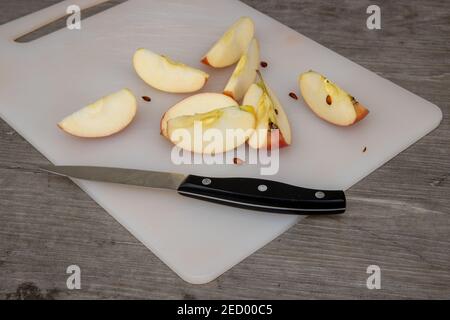 A plastic chopping board in a kitchen with a knife cutting up an apple Stock Photo