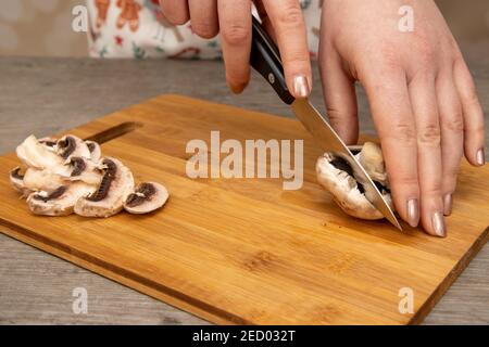 A woman in a kitchen cutting up a mushroom on a wooden chopping board, home cooking concept Stock Photo