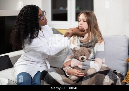 Child at the Pediatrician. Doctor's visit at home. Healthcare, child and medical concept. African woman doctor checking cervical lymph nodes of ill Stock Photo