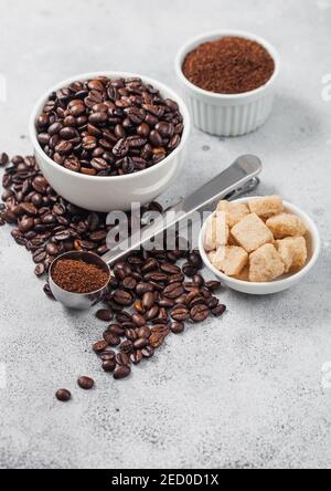 Fresh raw organic coffee beans in white bowl and powder on ligh table background with cane sugar and round steel scoop. Stock Photo