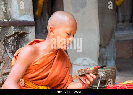 Siem Reap, Cambodia - April, 13,2018: Young monk reads mantras. Praying buddhist monk. Young boy in orange clothes of buddhist monk. Bold monk head. B Stock Photo