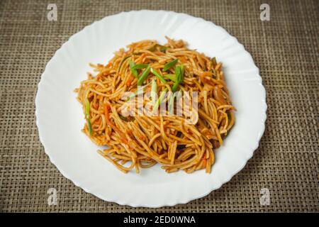 Veg Hakka Schezwan noodles served on a white plate with green onions. selective focus Stock Photo