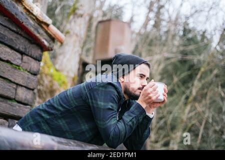 A hipster guy drinking coffee on the cottage terrace, melancholic autumn mood Stock Photo