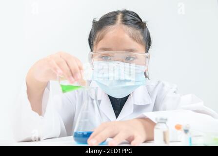 A little scientist is pouring green liquid chemical in Erlenmeyer flask isolated on white background. Science experiment and education concept Stock Photo