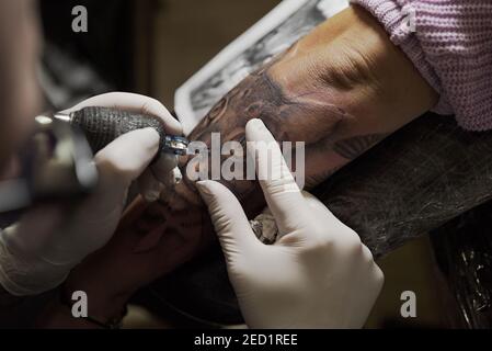 From above of unrecognizable male tattooist using machine and making tattoo on arm of crop client in salon Stock Photo