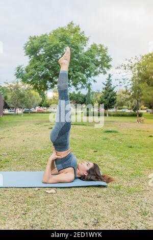 Side view of concentrated female balancing in Salamba Sarvangasana with raised legs on mat while practicing yoga in park Stock Photo