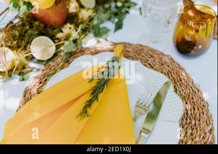 From above of plate with yellow napkin decorated with rosemary sprig placed on banquet table in garden Stock Photo