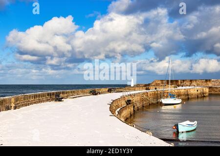 CULLEN BAY MORAY FIRTH SCOTLAND HARBOUR OR JETTY WALL COVERED IN SNOW WITH MOORED YACHT AND SMALL FISHING BOAT Stock Photo